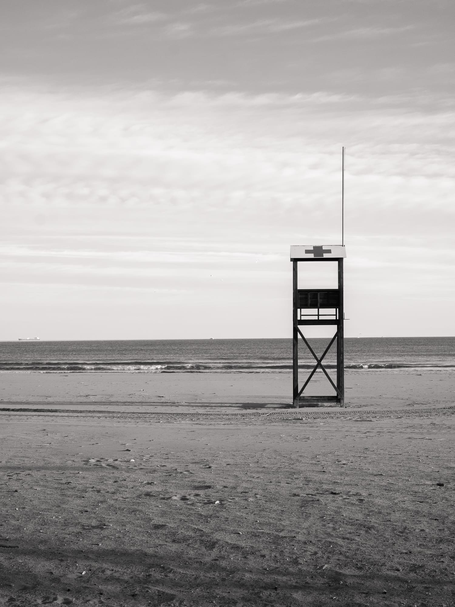 A volleyball net set on an empty beach, next to a short pylon, with the sea in the background.