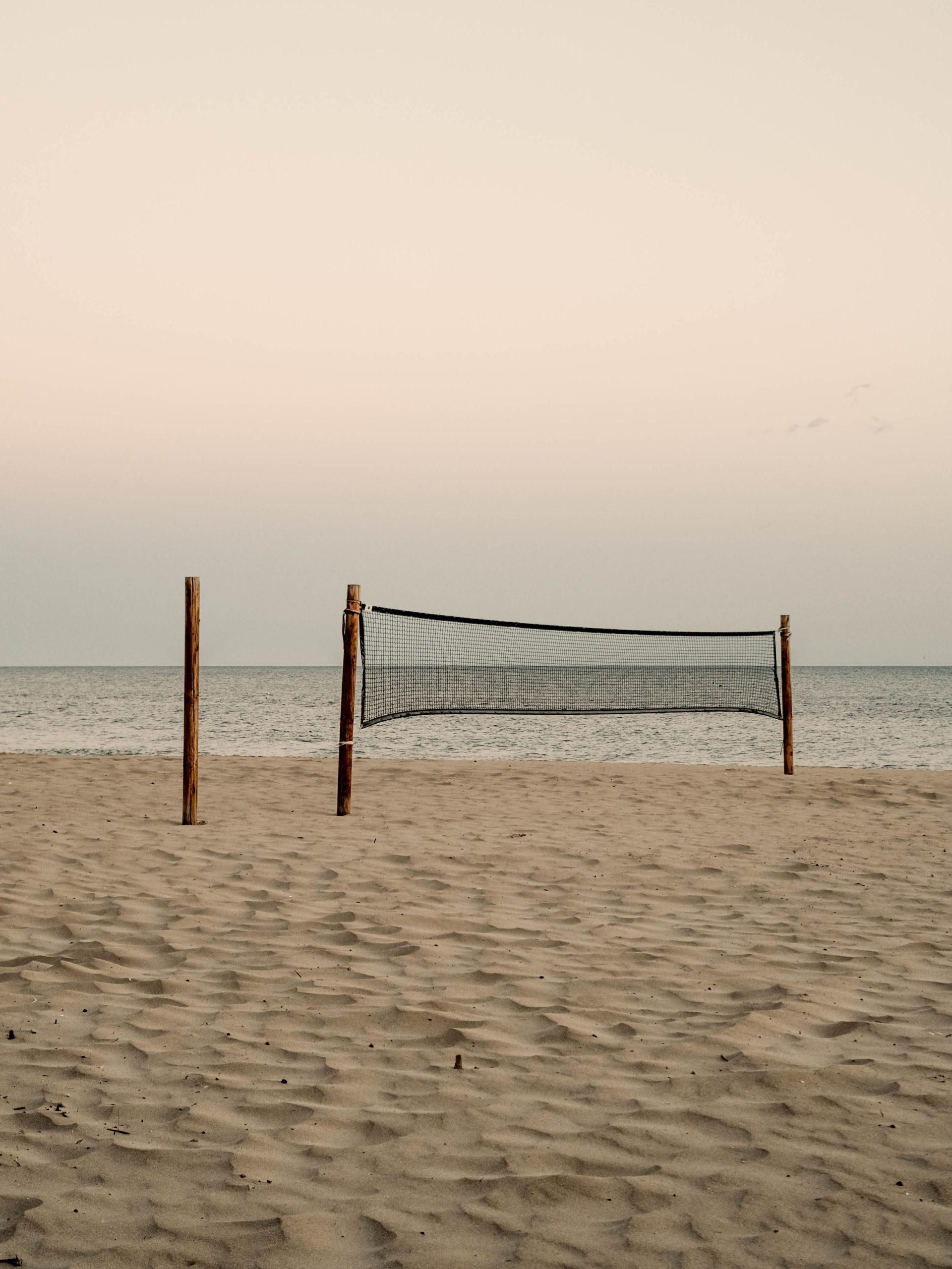 A volleyball net set on an empty beach, next to a short pylon, with the sea in the background.
